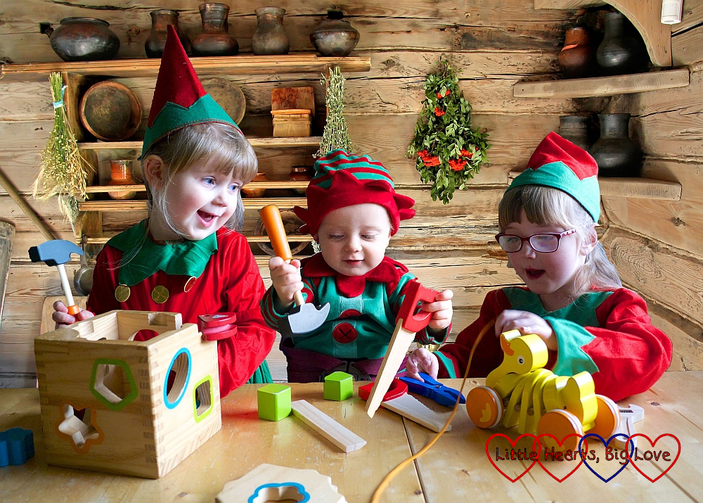 Sophie, Thomas and Jessica dressed as Christmas elves at the table together with a log cabin background
