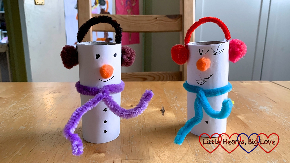 Two snowmen made from white paper covered toilet roll tubes with pipe cleaner and pompom scarves and earmuffs