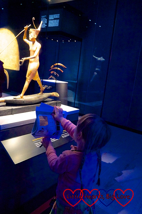 Sophie standing looking at a small statue of Tutankhamun while holding the children's activity trail sheet
