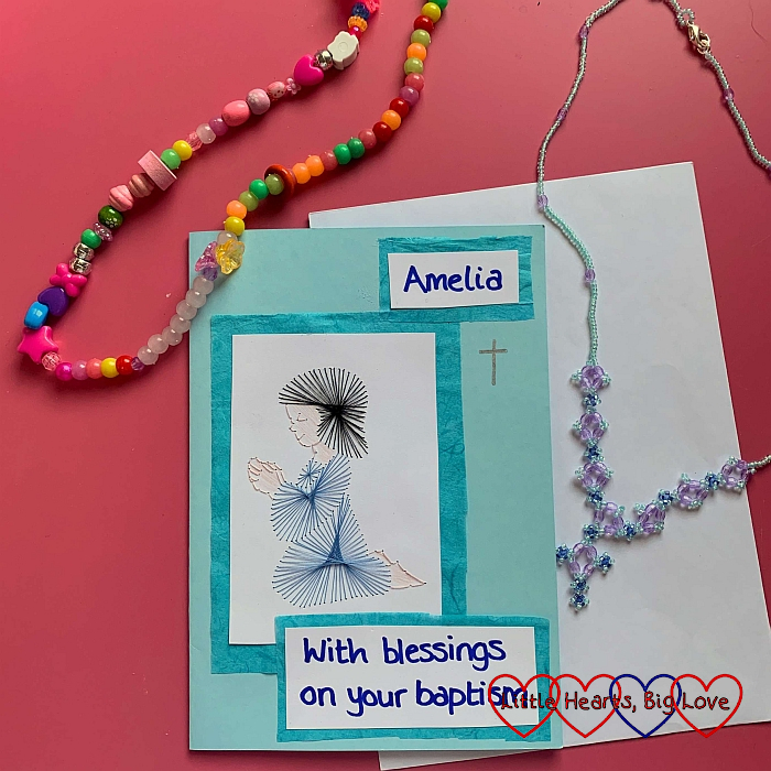 A hand-stitched card showing a little girl praying with a beaded necklace made with chunky beds and a beaded necklace with a cross made with seed beeds