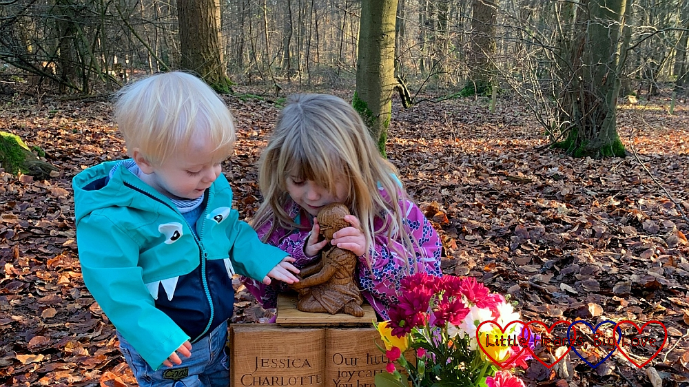 Thomas looking at the carving of Jessica on her memorial while Sophie gives it a hug