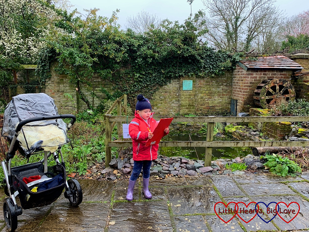 Sophie looking at her Beautiful Birds trail by the water wheel at Iver Environment Centre with Thomas in the buggy (with a rain cover on) next to her