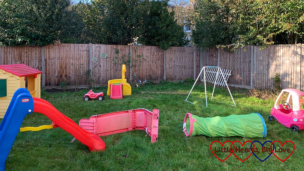An obstacle course made of slides, play tunnels, a trellis and the toy house set up in the garden