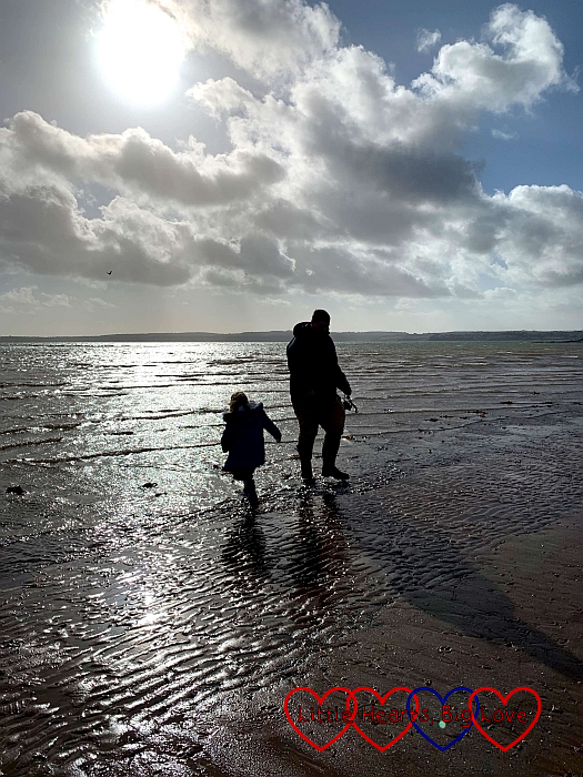 Sophie and Daddy in silhouette paddling in the sea in their wellies in Torquay