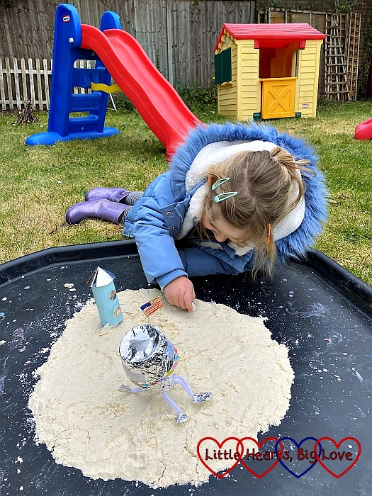 Sophie recreating with Moon landings on the tuff spot with a homemade rocket, lunar module and an astronaut on some moon sand