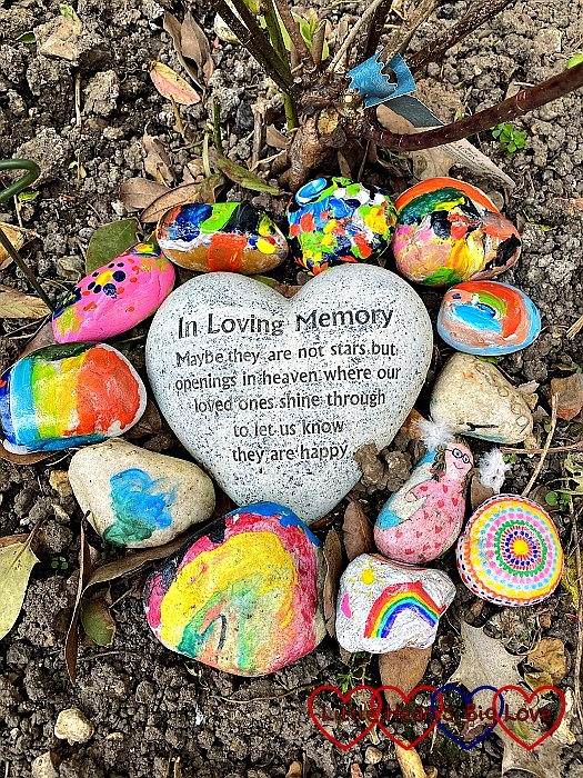 Colourful painted pebbles around a heart stone which says "In loving memory. Maybe they are not stars but openings in heaven where our loved ones shine through to let us know they are happy."