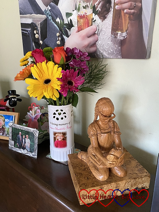 Rainbow-coloured flowers in a vase and a wooden carving of Jessica on top of my piano