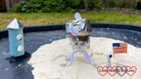 A toilet roll rocket, a tin-foil lunar module, a miniature American flag and a tiny astronaut on moon sand in a tuff tray
