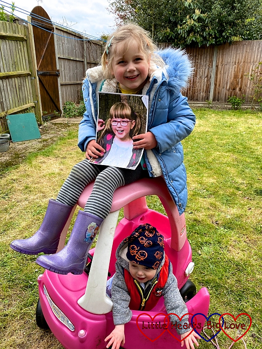 Sophie holding a photo of Jessica and sitting on top of the Little Tikes car with Thomas sitting inside it