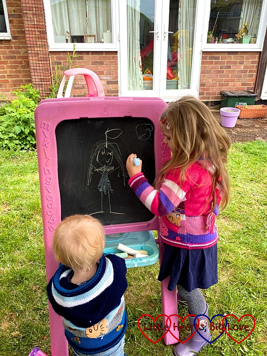 Sophie drawing a chalk picture of Jessica as an angel on her easel while Thomas watches