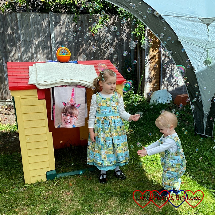 Sophie and Thomas standing by their playhouse, with Jessica's photo blanket hanging down from the roof and bubbles coming from the bubble machine on top of it