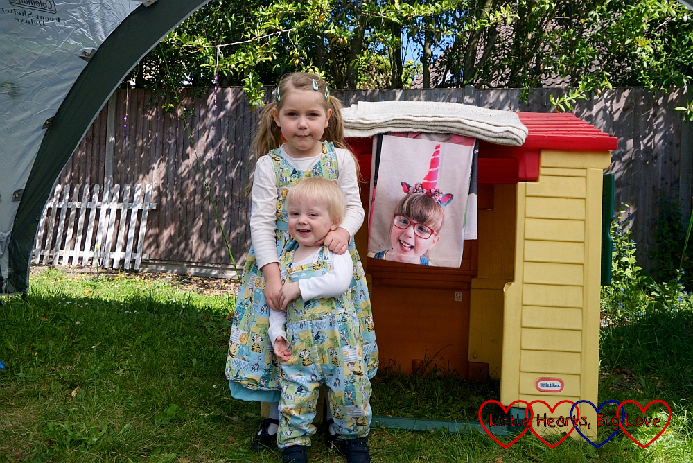Sophie and Thomas standing by their playhouse, with Jessica's photo blanket hanging down from the roof and bubbles coming from the bubble machine on top of it