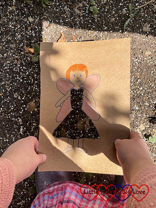 A picture of a fairy with the dress cut-out held against petal-covered soil