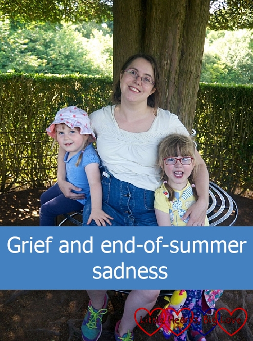 Me sitting on a bench in front of a tree with my girls either side of me - "Grief and end-of-summer sadness"