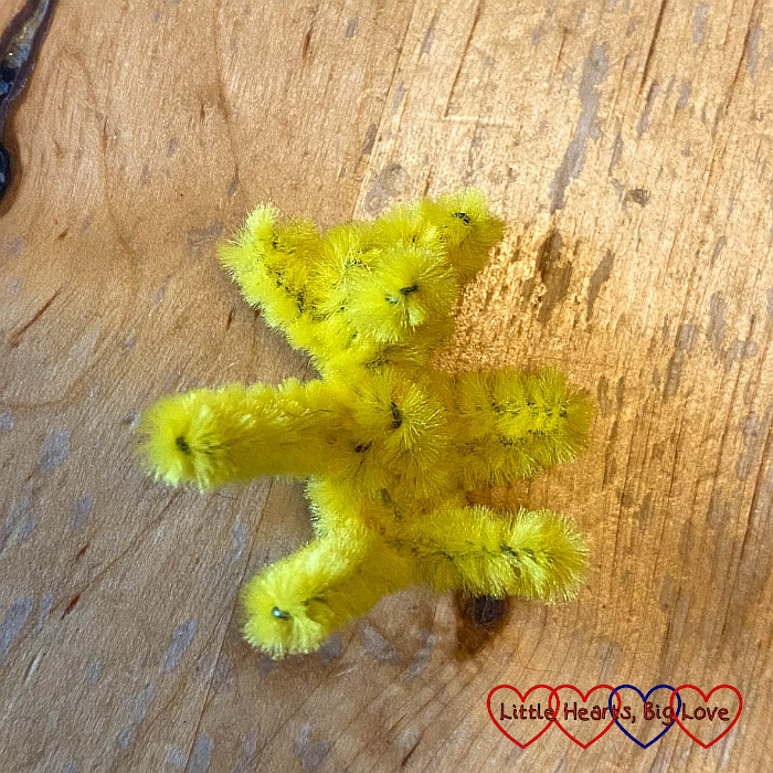 A tiny teddy bear made from a yellow pipe cleaner