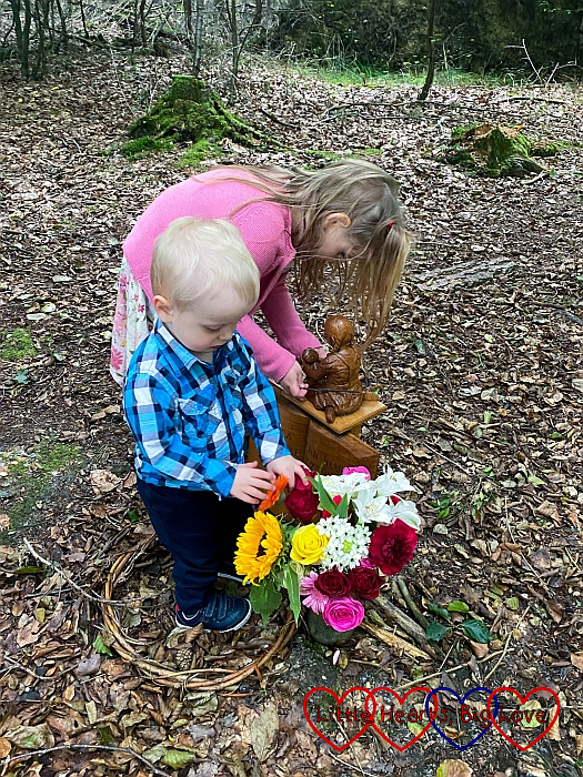 Sophie putting a twig on Jessica's carving and Thomas looking at the flowers at her forever bed