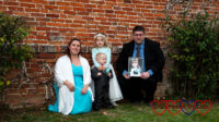 Me and Sophie in our bridesmaid dresses, Thomas in his page boy suit and hubby holding a photo of Jessica standing in front of a wall at my sister's wedding