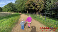 Sophie and Thomas walking hand-in-hand along a gravel path at Langley Park