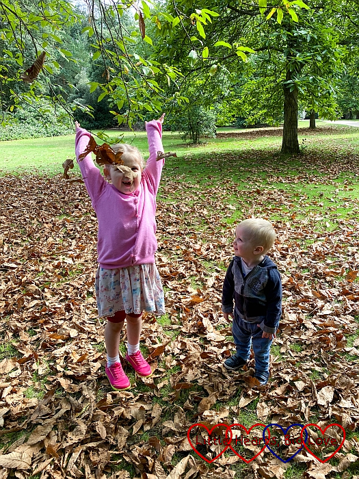 Sophie throwing leaves in the air with a smiley Thomas looking on