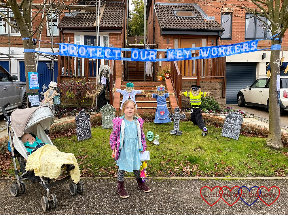 Sophie standing in front of a display featuring key worker inspired scarecrows and a banner reading "Protect our key workers"