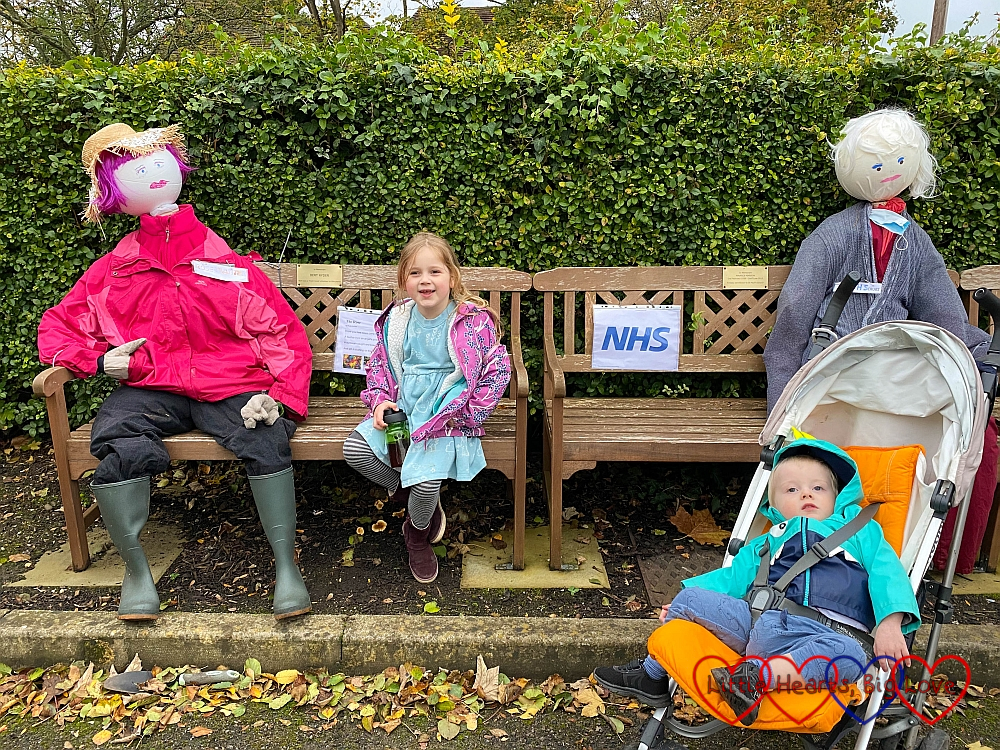 Sophie sitting between two scarecrows on a bench with Thomas in front in his buggy