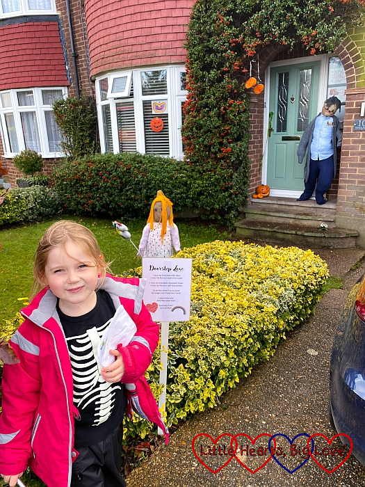 Sophie standing in front of a garden with one scarecrow in the garden looking at a scarecrow by the door
