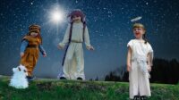 Sophie and Thomas dressed as shepherds with Sophie's toy goat and Jessica dressed as an angel against a starry sky background
