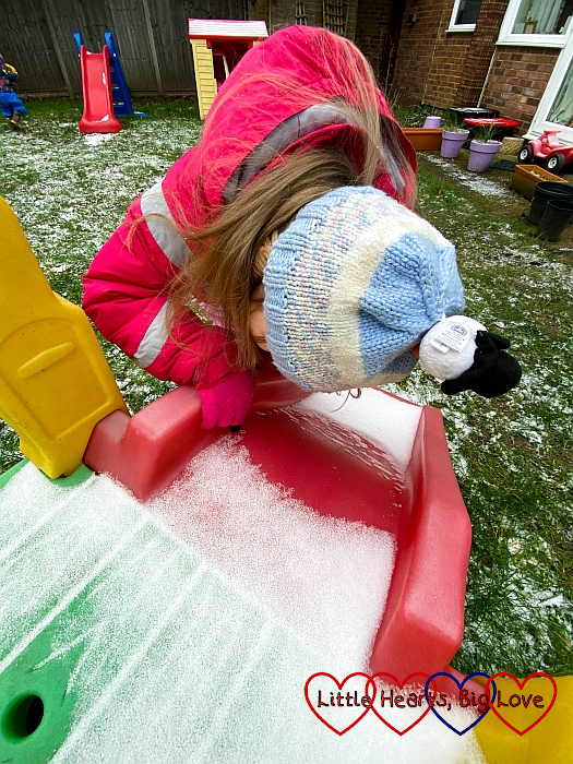 Sophie looking closely at the snow on her slide