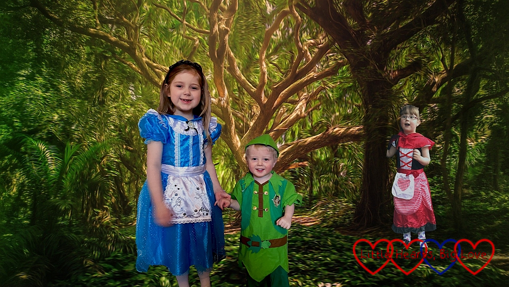 Sophie (dressed as Alice in Wonderland), Thomas (dressed as Peter Pan) with a forest background with Jessica (dressed as Little Red Riding Hood) peeping out from behind a tree