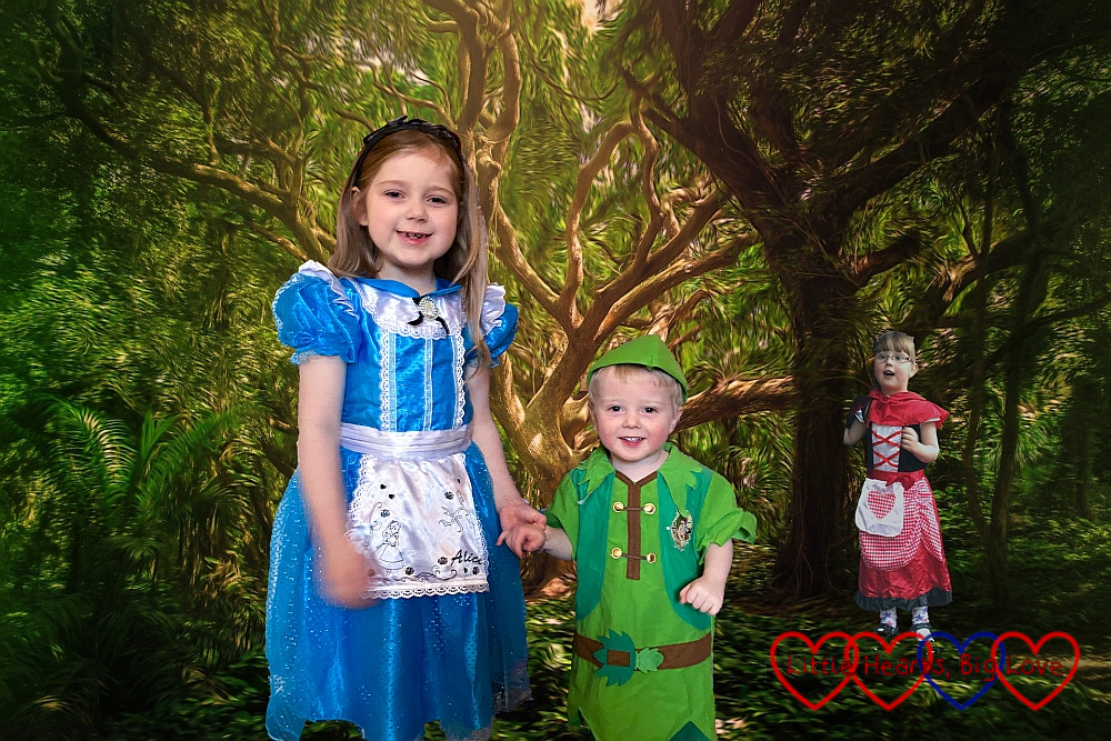 Sophie (dressed as Alice in Wonderland), Thomas (dressed as Peter Pan) with a forest background with Jessica (dressed as Little Red Riding Hood) peeping out from behind a tree