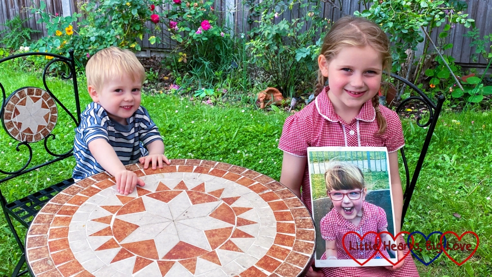 Sophie and Thomas sitting at the table in the garden with Sophie holding a photo of Jessica