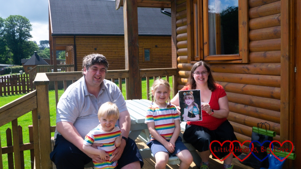 Hubby, Thomas and Sophie (in matching rainbow striped tops) and me (holding a photo of Jessica) outside our lodge at Coombe Mill