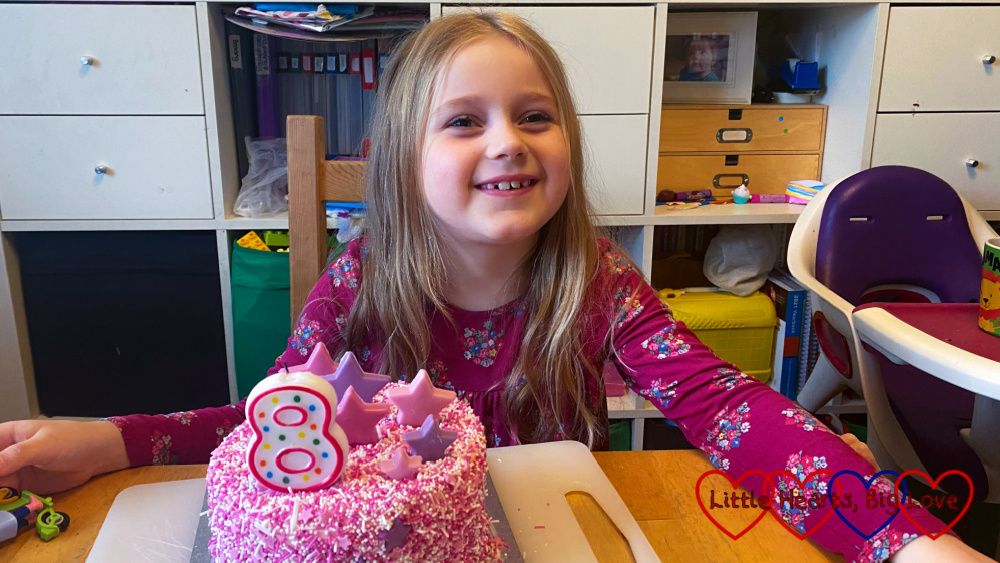 Sophie sitting at the table with a pink sprinkle-covered birthday cake with an '8' candle on top in front of her
