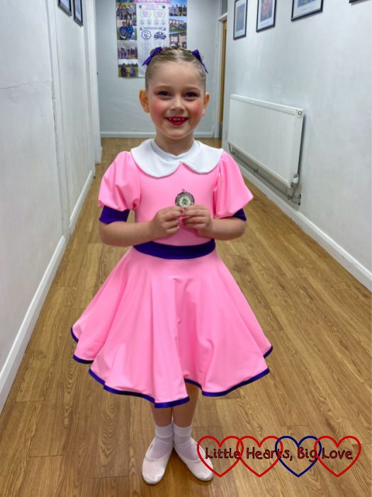 Sophie in a pink dress with purple sash and trim holding a medal for second place in her section in the dance festival