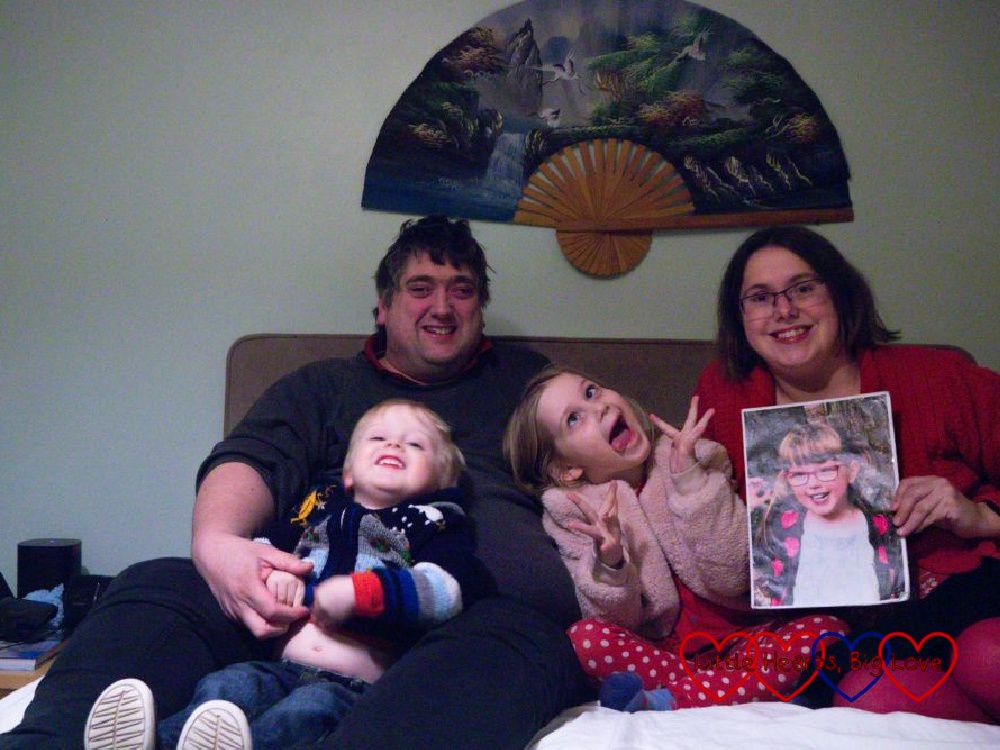 Me (holding a photo of Jessica), Thomas, Sophie and Daddy sitting on our bed with Sophie pulling a silly face