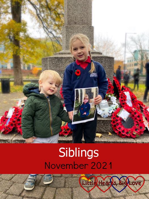 Sophie (holding a photo of Jessica on Remembrance Sunday) and Thomas standing in front of poppy wreaths on the peace memorial - "Siblings - November 2021"