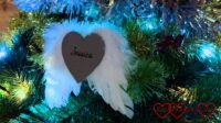 A decoration of a heart with 'Jessica' on it backed with angel wings on a Christmas tree