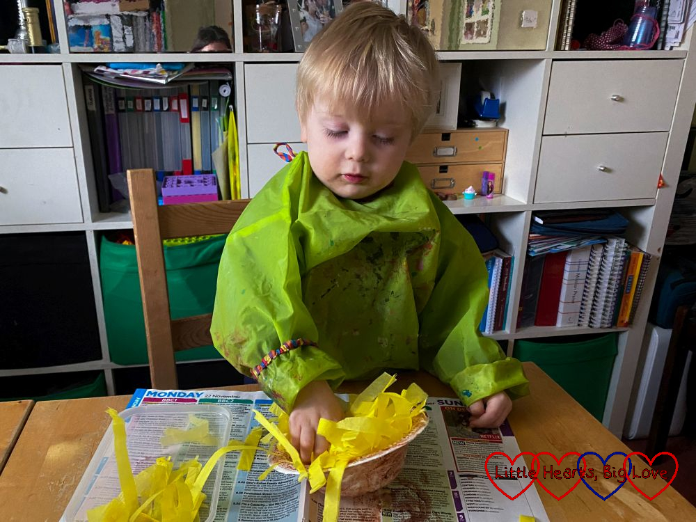 Thomas putting shredded yellow tissue paper into a brown-painted paper bowl