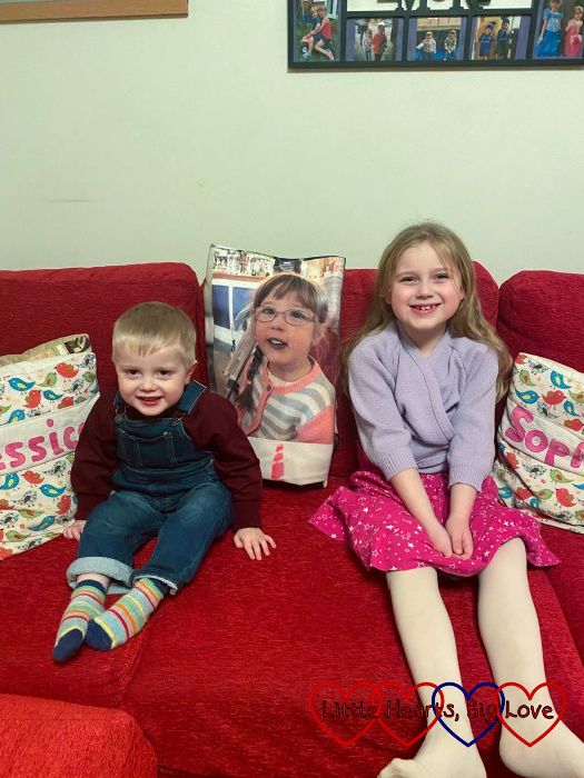 Thomas and Sophie sitting on a red sofa with a 'Jessica' cushion one side and a 'Sophie' cushion the other, and Jessica's picture on her photo blanket in between them