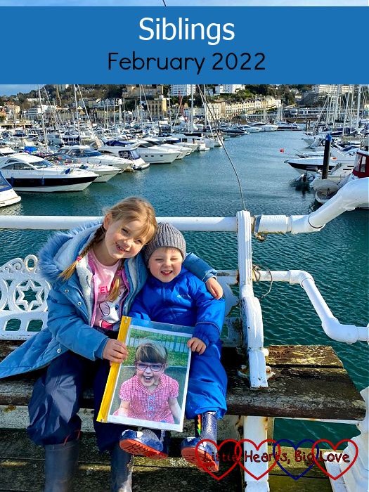 Sophie and Thomas sitting on a bench on the pier at Torquay with boats on the water behind them and them both holding a photo of Jessica - "Siblings - February 2022"