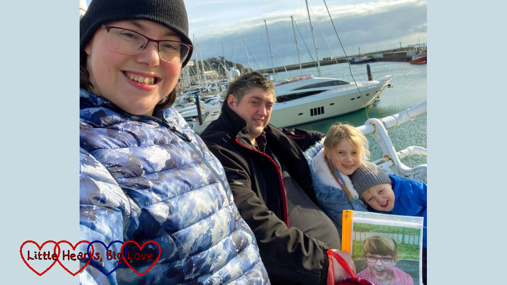 Me, my husband (holding a photo of Jessica), Sophie and Thomas sitting on a bench at Torquay with the sea and boats in the background