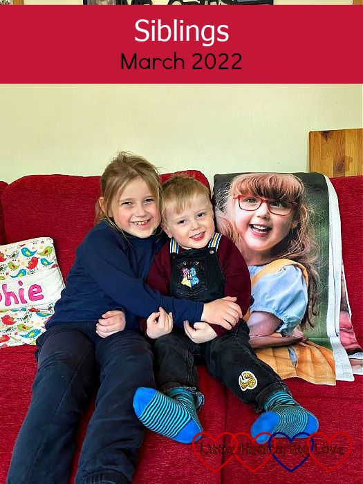 Sophie and Thomas sitting on the sofa with an image of Jessica from her photo blanket draped on the sofa behind them. There is a cushion that says 'Sophie' next to Sophie and another one that says 'Jessica' on the opposite side, next to the photo of Jessica - "Siblings - March 2022"