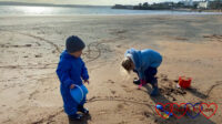 Sophie and Thomas wrapped up in winter coats playing on the beach at Torquay