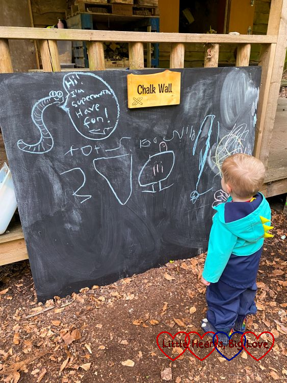 Thomas writing 'at Tots Go Wild' on a chalkboard under a picture of Superworm with the caption "Hi I'm Superworm. Have fun!"