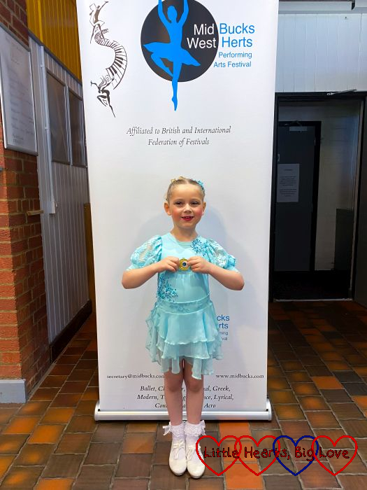Sophie standing in front of a 'Mid Bucks and West Herts performing arts festival' banner holding a gold medal