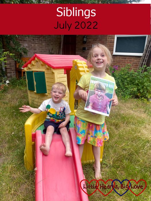 Sophie standing next to the little slide in the garden holding a photo of Jessica and Thomas sitting at the top of the slide - "Siblings - July 2022"
