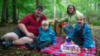 My husband, Thomas, me and Sophie sitting on a picnic blanket at Jessica's forever bed with her Twilight Sparkle unicorn birthday cake on the picnic blanket in front of us