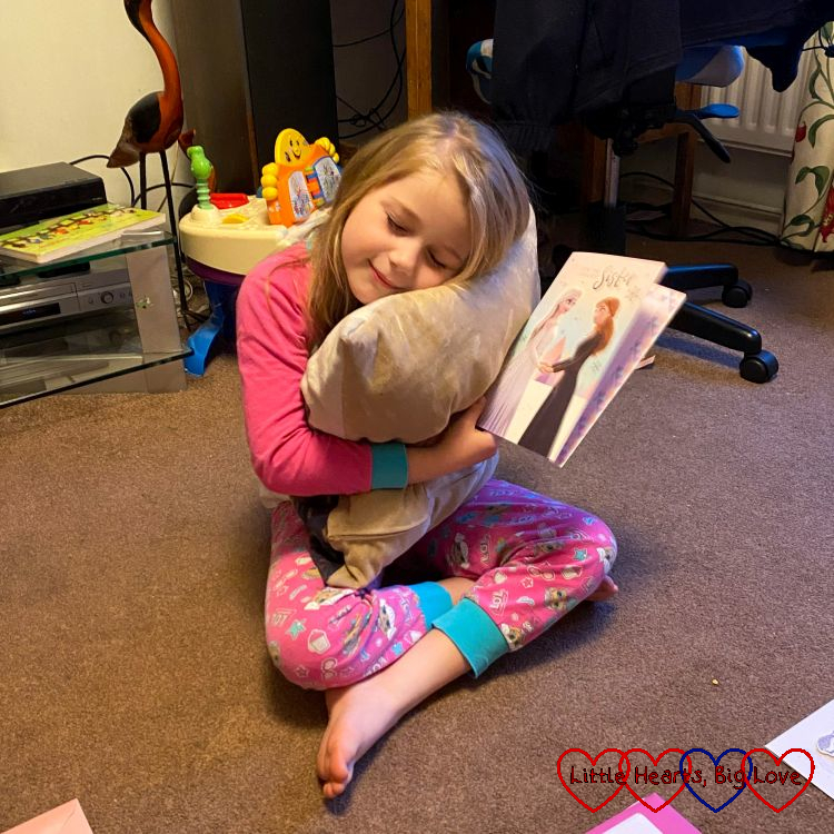 Sophie holding a 'sister' birthday card and cuddling Jessica's photo cushion