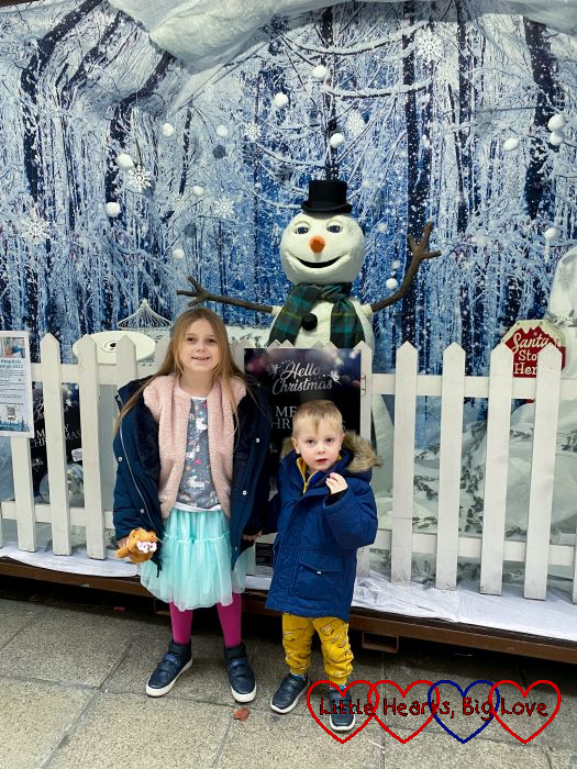 Sophie and Thomas standing in front of a snowman at the Christmas market