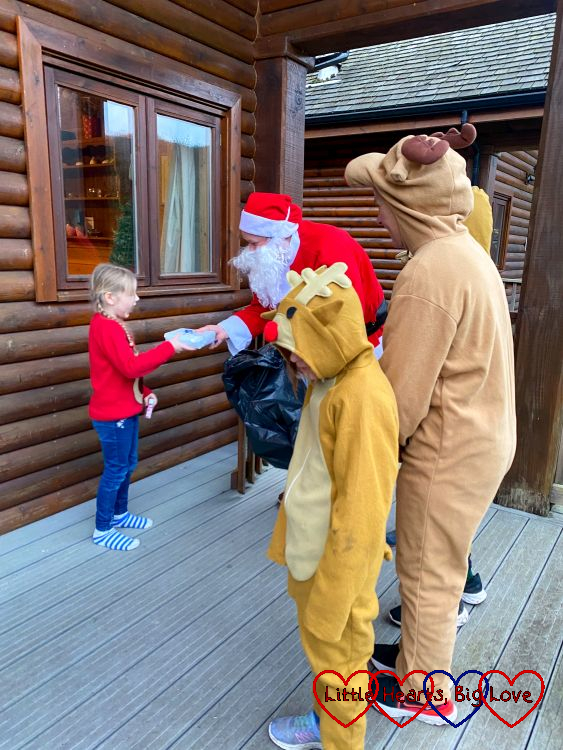 Sophie receiving a present from Father Christmas accompanied by four people dressed in reindeer onesies